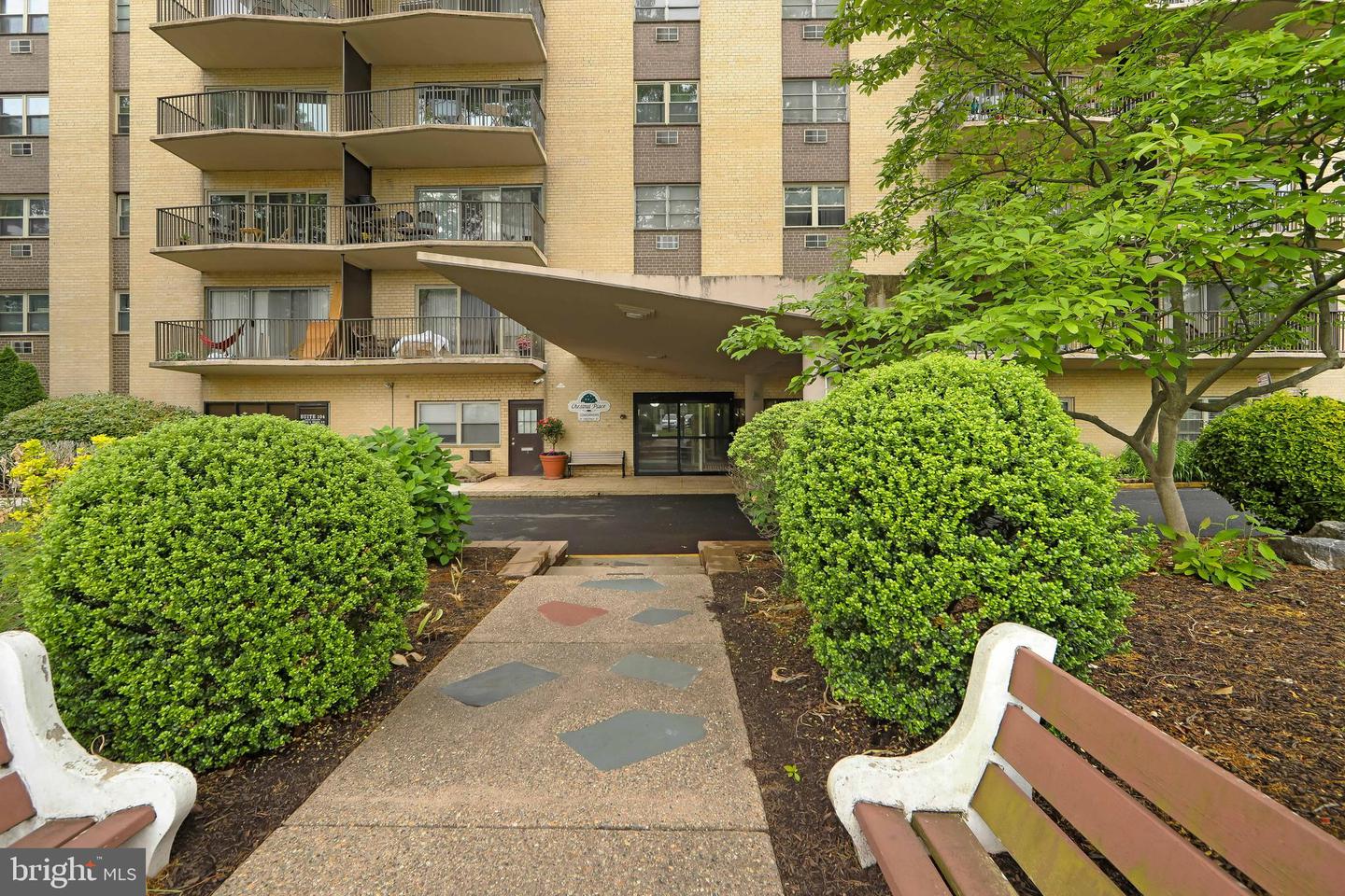 Apartment building entrance with benches and bushes.