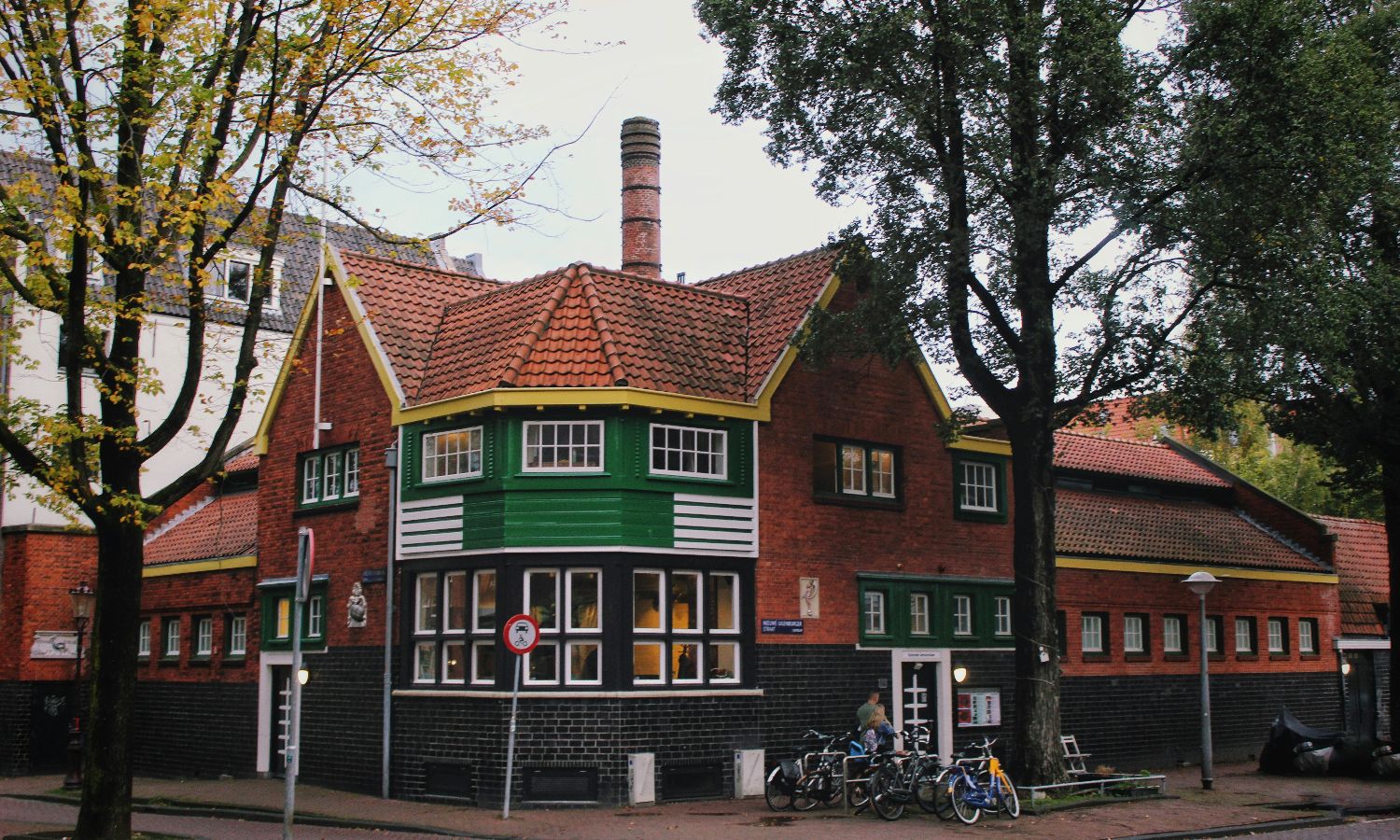 Charming brick house with green accents and bicycles outside on a tree-lined street.