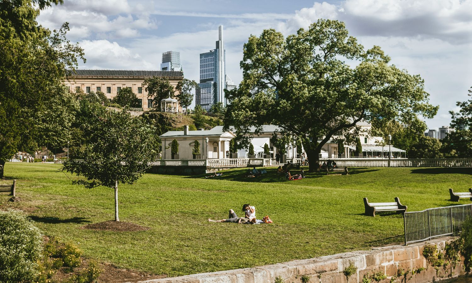 People relaxing on a grassy park with city buildings in the background.