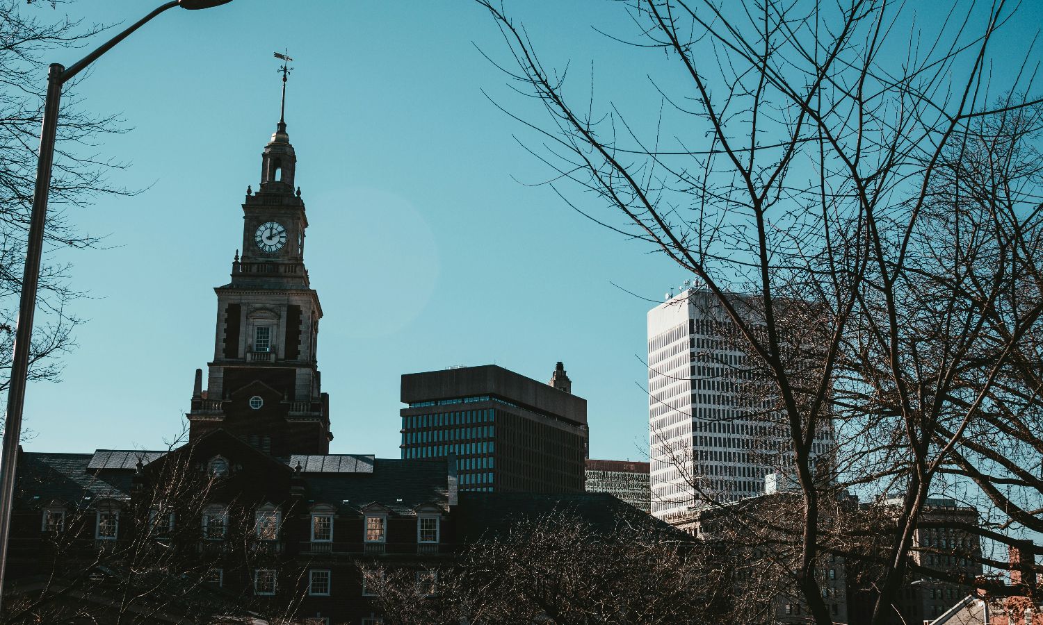 A city skyline featuring a historic clock tower and modern buildings under a clear sky.